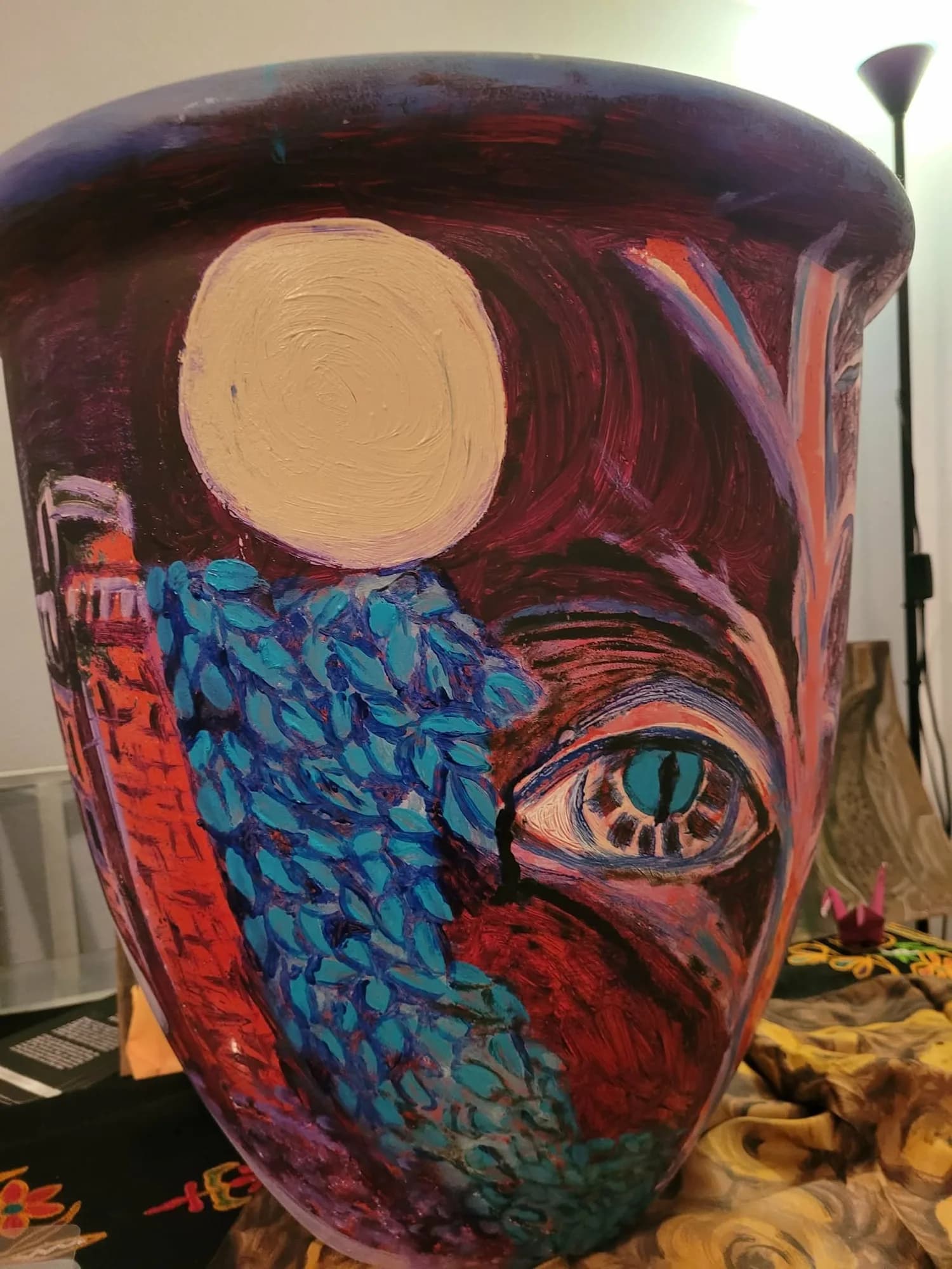 A painted plant pot with a pale moon, blue leaves and a watchful eye