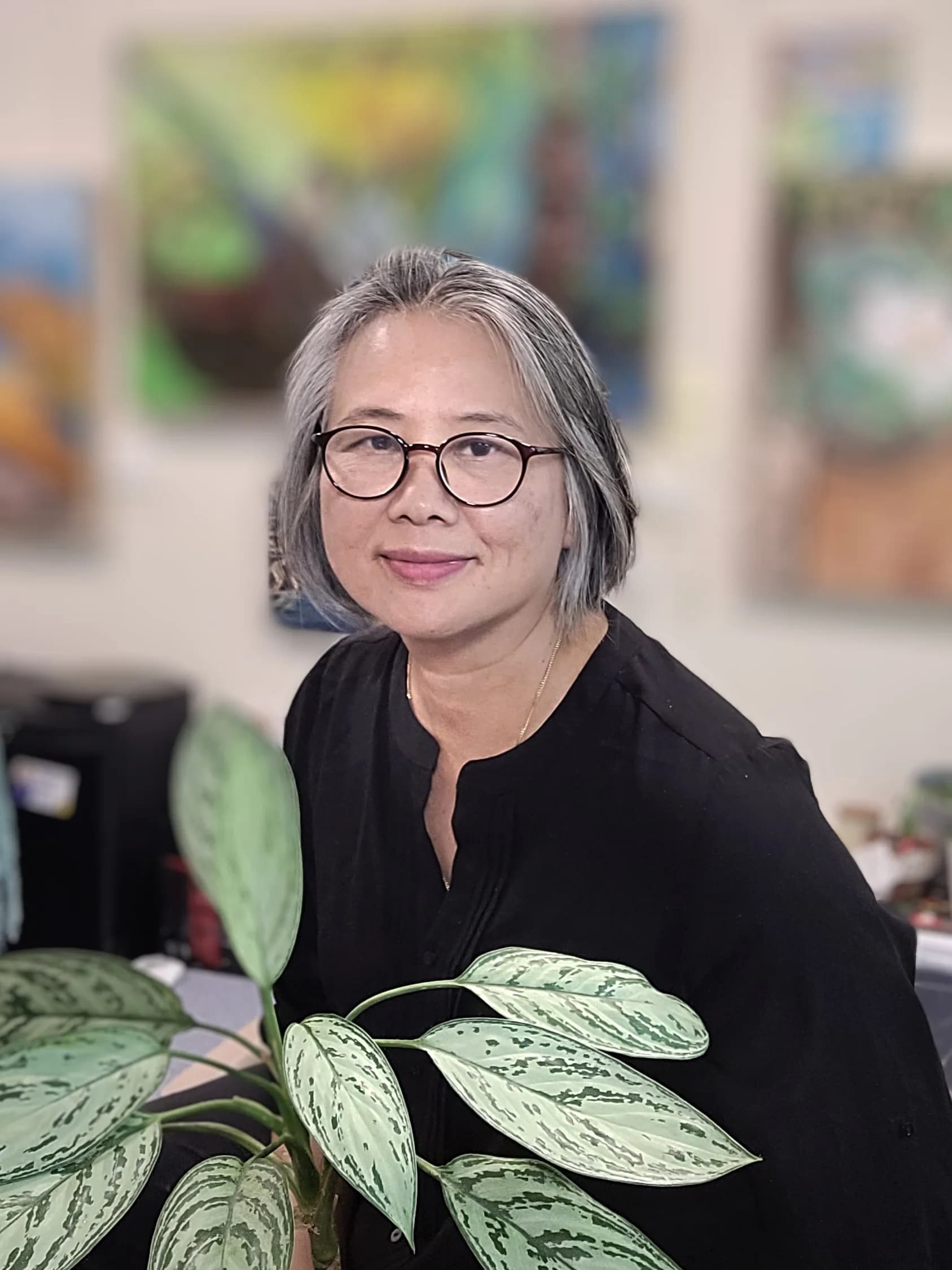 Daw Mi smiling, with her paintings softly blurred behind her