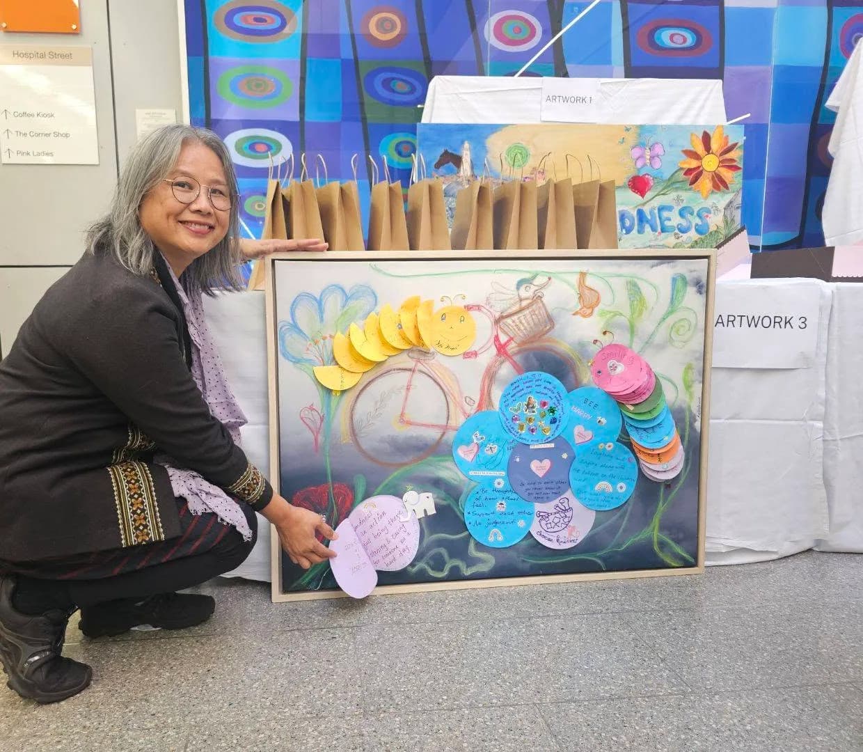 Daw Mi at Royal North Shore Hospital beside a painting created with patients, visitors and staff